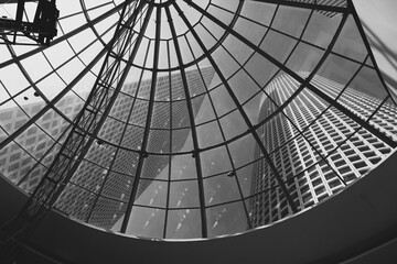 Overhead view of a radial glass ceiling with a skyscraper's patterned facade beyond.
