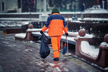 Worker sweeps street, janitor with broom, dustpan collect garbage in plastic bag during snow storm....