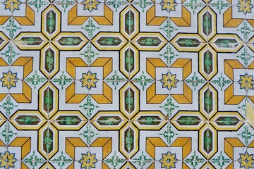 Aged ceramic tiles of faded yellow colour with geometric ornament on the weathered shabby facade in...