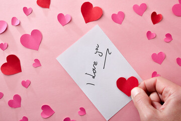 Romantic note and hand with a heart on pink background