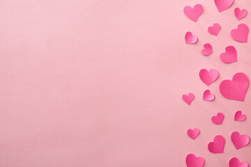 Love background with fuxia pink heart cutouts of various sizes on the right edge isolated on a pink...