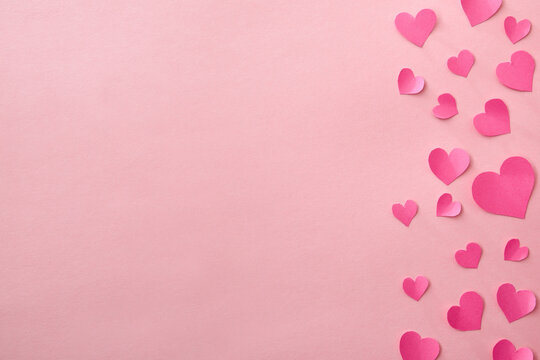 Love background with fuxia pink heart cutouts of various sizes on the right edge isolated on a pink background