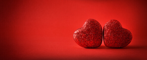 Love background with two red glitter hearts on red background