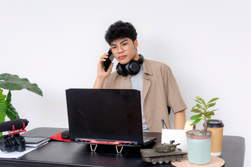 Creative young freelancer discusses project on phone, using a black gaming laptop in a modern...