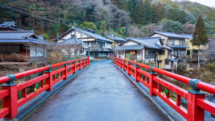 Narrow red bridge leads to traditional houses in Japanese village - 719134209