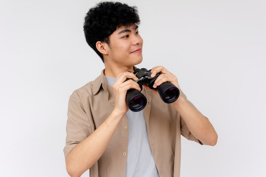 Joyful young Asian man with binoculars looking around his surroundings. Cheerful expression suggesting anticipation or discovery.