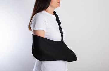 A girl in white with a fixing black bandage on her arm after an injury, a fracture of the radius...