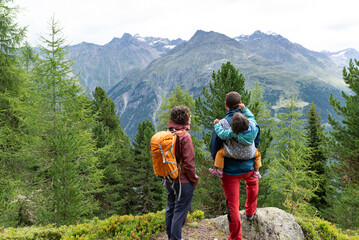 Back view of a family with little daughter in a baby carrier at his back enjoying views during a hiking day in Sölden,  Austrian Alps.