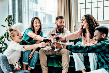 Young people having fun drinking red wine on sofa at house - Multicultural gathering of adult...