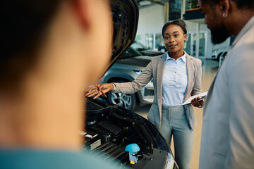 Young black saleswoman selling car while working in showroom.