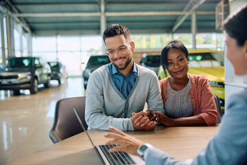 Young couple and car saleswoman using laptop in showroom. - obrazy, fototapety, plakaty