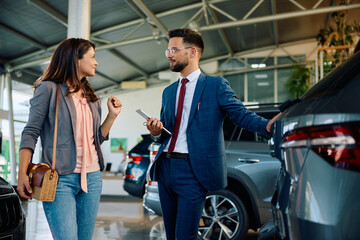 Car salesman and his female customer talking in showroom.