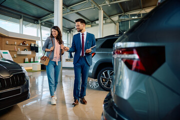 Happy woman buying new car with help of salesman in showroom.