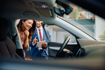 Happy woman buying new car in showroom.