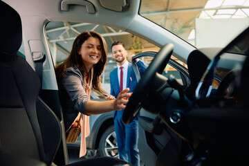 Happy woman looking at car interior while shopping in showroom.