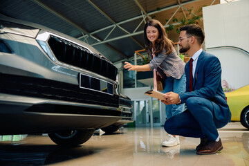 Happy woman choosing new vehicle with help of salesman at car dealership.