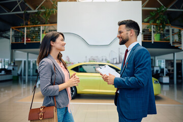Happy salesman and his female customer talking at car dealership.