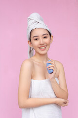 A young asian woman wrapped in a towel holding a blue deodorant body soap. Bath and body care concept. Soft pInk background.