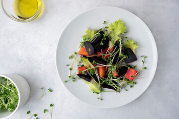 A healthy salad made from boiled beets, carrots, micro greens and lettuce. Dish on a light gray...