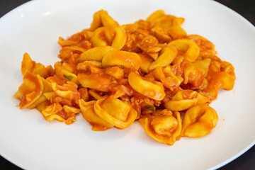 Traditional stuffed capeletti pasta with tomato sauce served on a white plate.