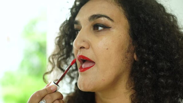 Close-up middle aged woman with black hair applies red lipstick. Oriental woman doing bright makeup in front of the mirror 4K