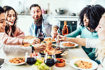 Happy ethnic group of friends eating pasta at home lunch party - Cheerful young people having dinner break together in italy - Life style concept with guys and girls in day of celebration