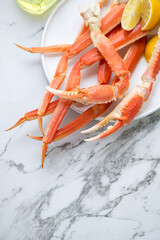 Plate with boiled crab legs and claws on a white marble background, vertical shot with space, selective focus, elevated view