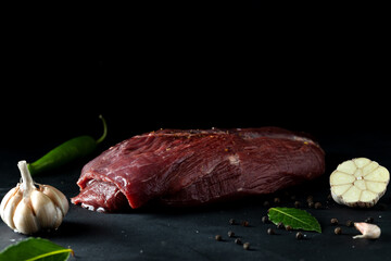 A large piece of venison on a cutting black board with spices, close-up