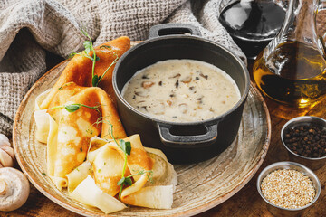 Pancakes with mushrooms and cheese in a saucepan on a wooden background