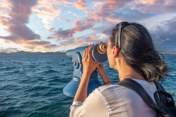 A young woman looks through a telescope at the seashore.