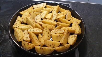 Sliced raw potatoes are mixed with seasonings are placed in a black tray, Roasted potatoes Menu.
