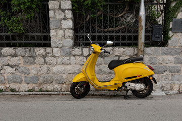 Kotor, Montenegro - 06 17 2023: A yellow scooter parked against the stone wall at Dobrota's promenade 