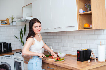 Beautiful woman in a white T-shirt and blue jeans prepares a healthy breakfast in the kitchen - 719238057