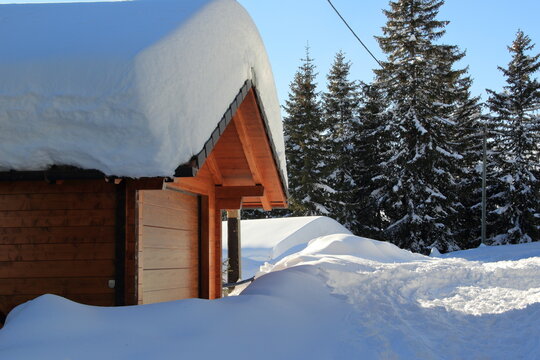 Chalet di Legno con neve sopra il tetto e pini sullo sfondo