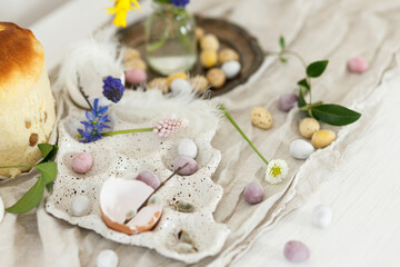 Obraz na płótnie Canvas Colorful easter chocolate eggs, easter bread, spring flowers and linen cloth on rustic wooden table. Easter modern simple decoration and homemade traditional cake. Happy Easter!