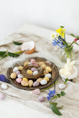 Obraz na płótnie Canvas Stylish easter chocolate eggs in nest, spring flowers, feathers and linen cloth on rustic wooden table. Easter modern simple decoration still life. Happy Easter!