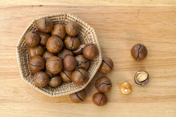 Top view of basket of roasted macadamia seeds on a wooden table with macadamia nuts spread out. The seeds have flavor and a fragrant texture Rich in many nutrients. 