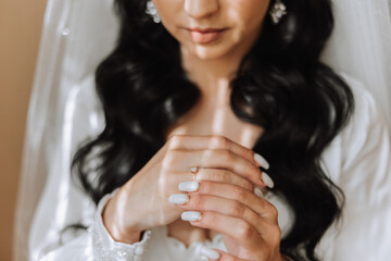 Hands of the bride in a white wedding dress with a gold wedding ring with a diamond close-up. Wedding photo