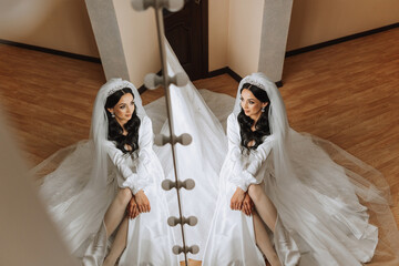 A beautiful bride is sitting in a dressing gown in the morning before the wedding ceremony in a...