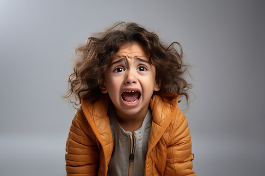 A girl in an orange jacket screams scaredly at the camera on a gray background