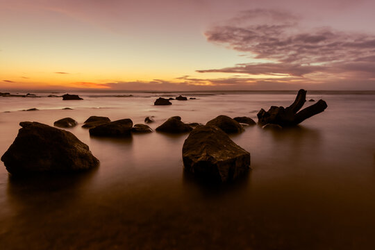 Sonnenaufgang mit Felsen im Vordergrund und sanften Wasser am Ostsee Bodden