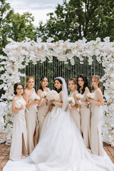A brunette bride and her bridesmaids in matching cream dresses stand and rejoice with bouquets of...