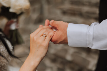 Groom holding bride's hand, cropped photo. Details at the wedding. Gold wedding rings on hands. High quality photo.