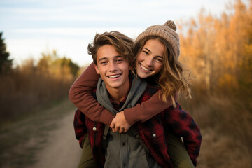 Two happy smiling young students teenagers in love have romantic walk outside in autumn park. Girl rides her boyfriend's back look into camera