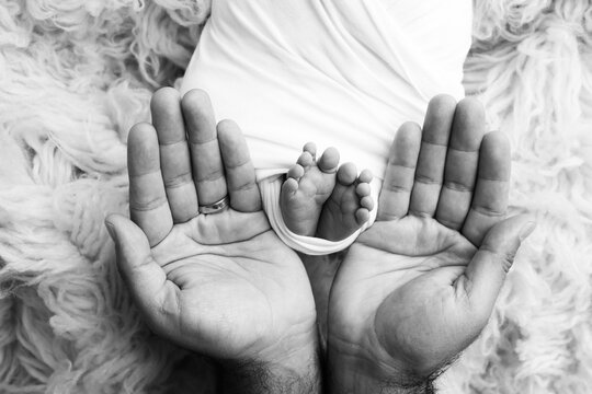 The palms of the father, the mother are holding the foot of the newborn baby. Feet of the newborn on the palms of the parents. Studio macro black and white photo of a child's toes, heels and feet.