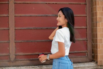 Teenage girl dressed in vintage clothes Including a white t-shirt and pants. standing behind the wall smiling