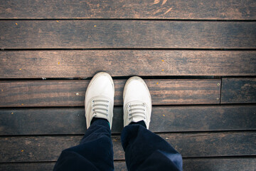 Top of legs in jeans and white sneakers on wooden table on wooden background in vintage tone and copy space concept.
