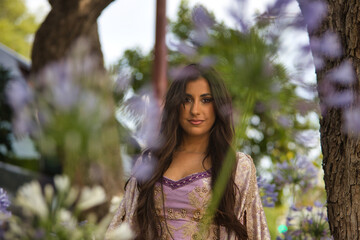 Young, Hispanic, pretty, brunette woman in an elegant vintage violet dress, seen through violet flowers. Concept of beauty, fashion, trend, elegance, spring.