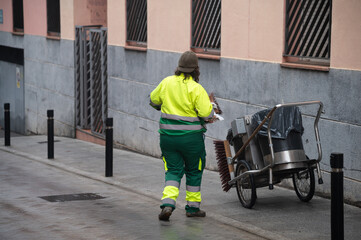 Una operaria municipal de limpieza con su escoba y recogedor limpia en una calle de una ciudad española.