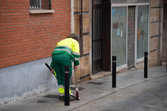 Una operaria municipal de limpieza con su escoba y recogedor limpia en una calle de una ciudad espa&ntilde;ola.